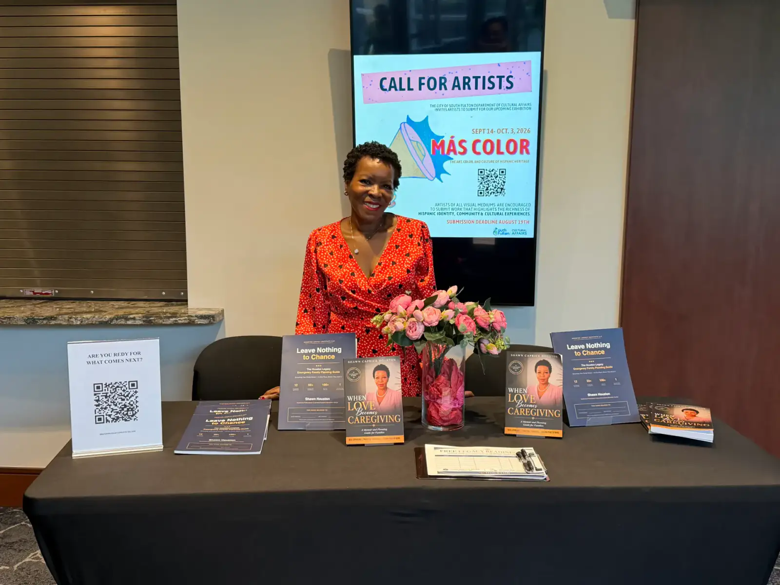 Shawn Caprice Houston behind a display table of her books at a community event, with an event poster behind her