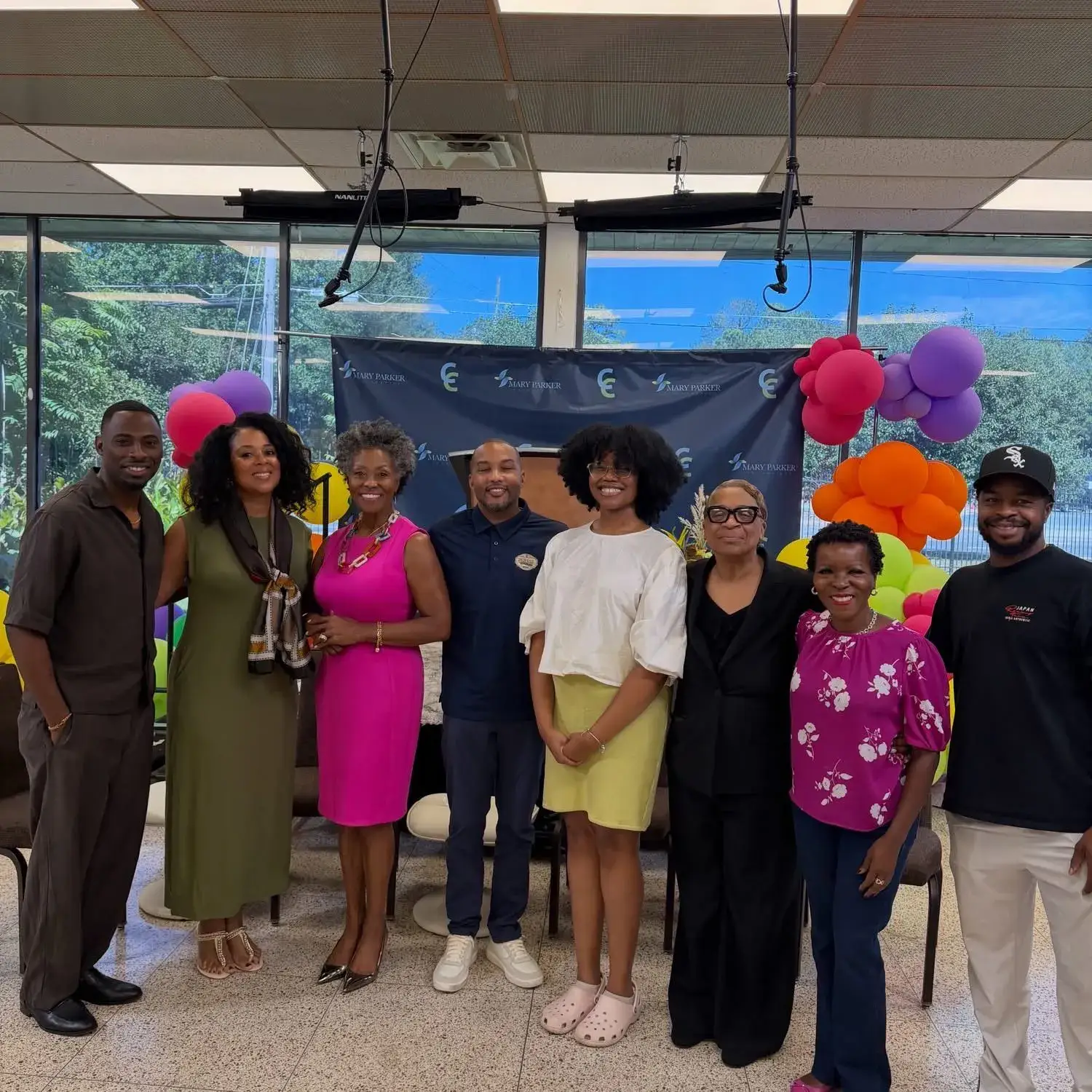 Shawn Caprice Houston with a group of community partners beneath a backdrop decorated with colorful balloons