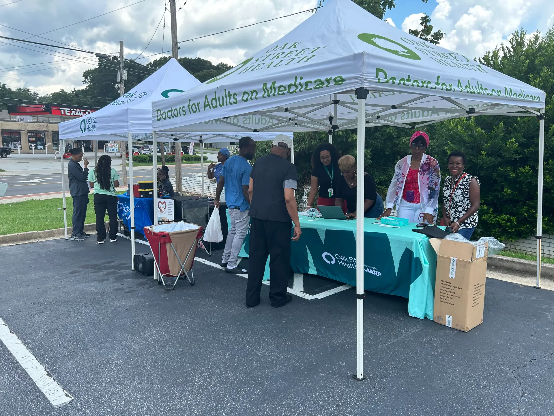 Shawn Caprice Houston smiling with community participants beside Oak Street Health outreach tents and information tables